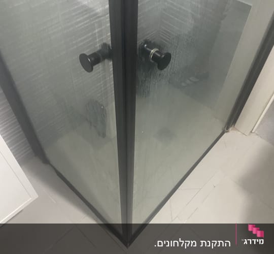 מקלחון זכוכית עם ידיות שחורות על רצפת אריחים